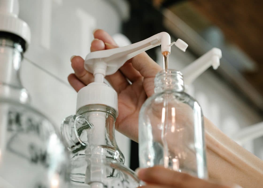 Hands refilling a glass bottle from a pump dispenser.