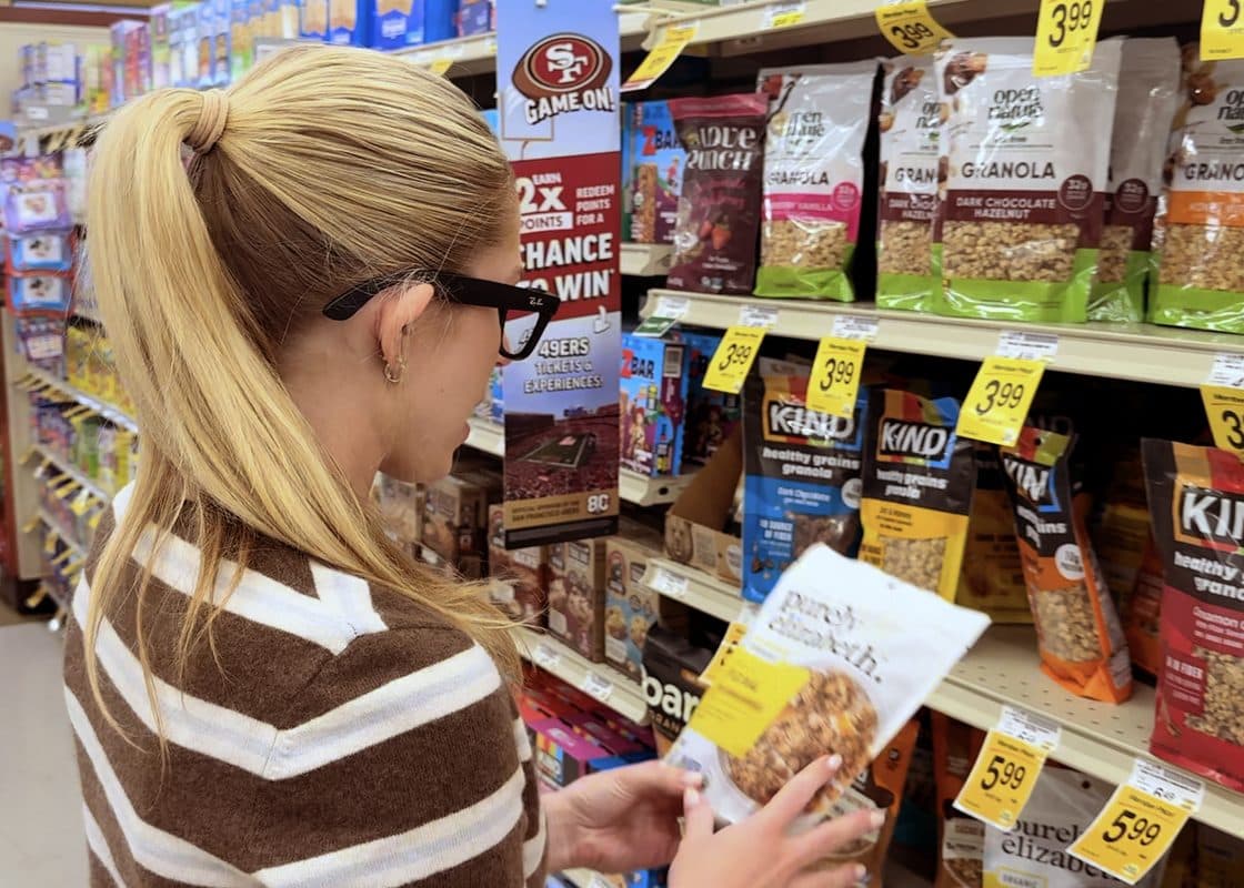 A shopper reaching for a product on a grocery store shelf.